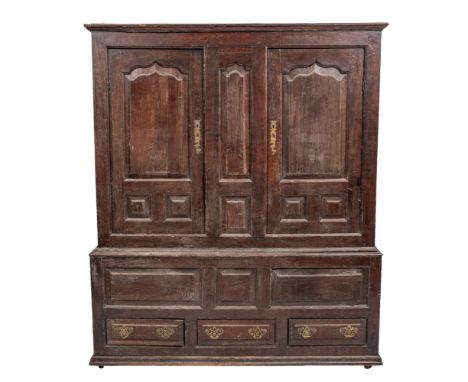 A George II oak linen cupboard, mid 18th century; the cornice above two panel doors with shallow Gothic arches, flanking a ce