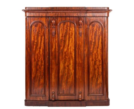 A Victorian mahogany compactum wardrobe, circa 1870; with moulded breakfront cornice above three arched panel doors intersper