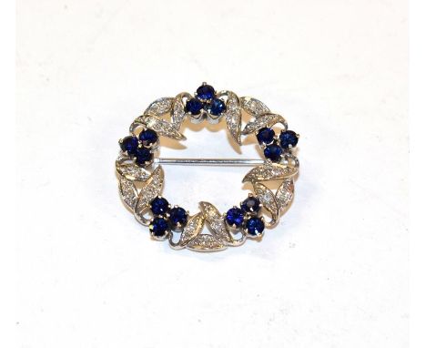 A sapphire and diamond brooch, realistically modelled as a wreath, clusters of three round cut sapphires alternate with leaf 