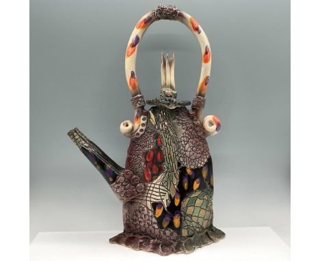 Tall whimsical teapot with raised tile design, applied spout and tall arched handle. Piece is completed in multicolor includi
