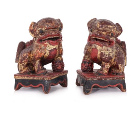 A PAIR OF LARGE CARVED WOOD FOO DOGS
19th-Early 20th Century, typically modelled with one leg resting on a ball, red lacquere