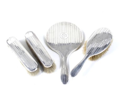 A silver four piece dressing table set. Each with engine turned bands and round reserves with a gothic monogram, comprising; 