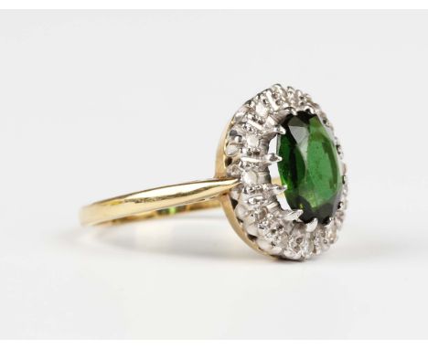 An 18ct gold ring, claw set with an oval cut green tourmaline within a surround of circular cut diamonds, London 1963, weight