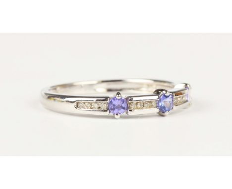 A 9ct white gold, tanzanite and diamond half hoop ring, claw set with three circular cut tanzanites alternating with four row