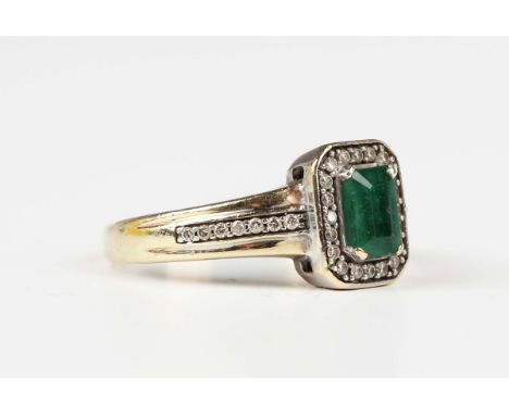 A 9ct gold, emerald and diamond cluster ring, claw set with the cut cornered rectangular step cut emerald within a surround o