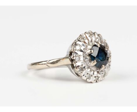 A white gold, sapphire and diamond cluster ring, claw set with the circular cut sapphire within a surround of circular cut di