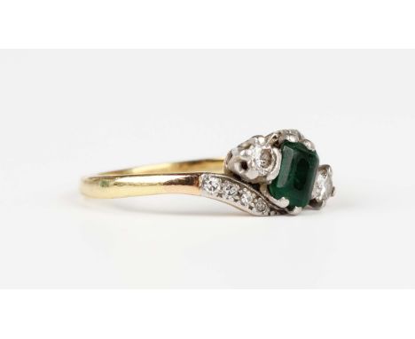 A gold, emerald and diamond ring in a crossover design, claw set with the cut cornered rectangular step cut emerald between t