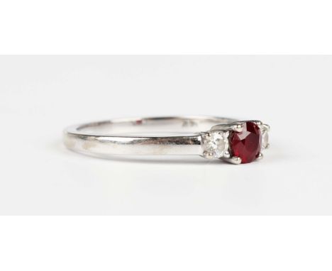 A white gold, treated ruby and diamond three stone ring, claw set with the circular cut treated ruby between two circular cut