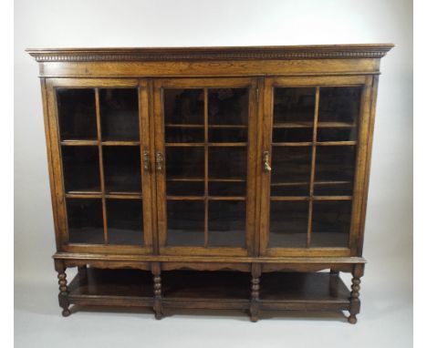 An Edwardian Oak Glazed Three Section Bookcase on Short Bobbin Supports Over Stretcher Shelf. 154x37x130cm High 