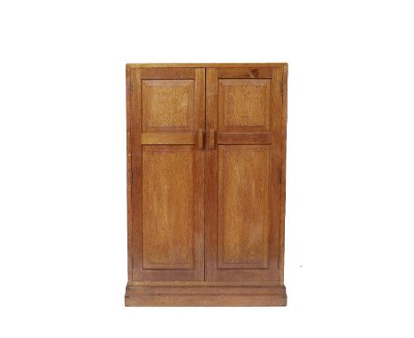 In the manner of Heals An oak cupboard/small compactum, the panelled doors enclosing shelf space, on plinth base, 119cm high,