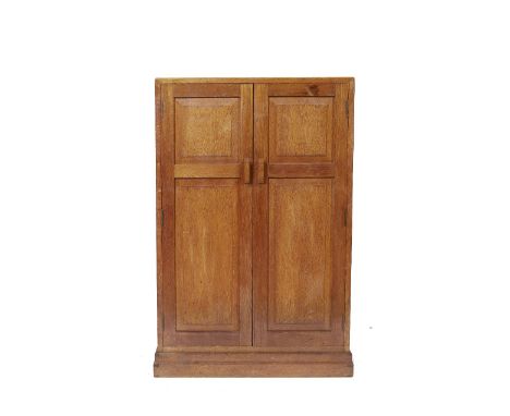 In the manner of Heals An oak cupboard/small compactum, the panelled doors enclosing shelf space, on plinth base, 119cm high,