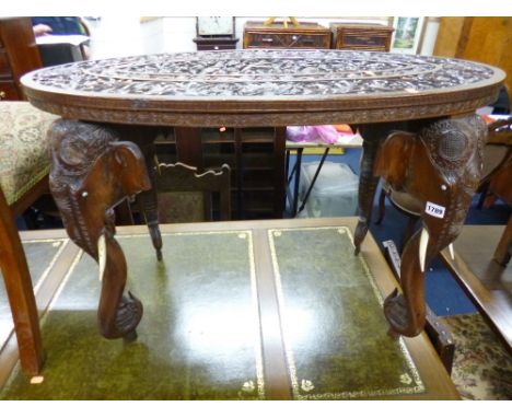 AN ORIENTAL STYLE OVAL COFFEE TABLE, heavily carved with elephant trunk supports