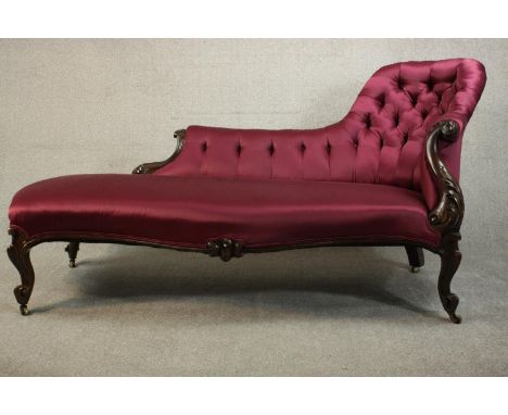 A Victorian show wood spoon back chaise longue with a button back upholstered in purple satin and carved scrolling arms, on c