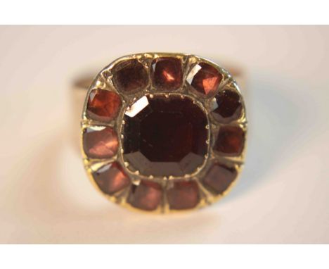 A Georgian yellow metal and foil backed garnet cluster ring. Set to the centre with a cushion shaped mixed cut garnet surroun