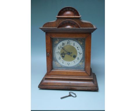 AN EDWARDIAN OAK CASED MANTEL CLOCK WITH SILVERED DIAL, the architectural case with carved detail, the movement striking on a