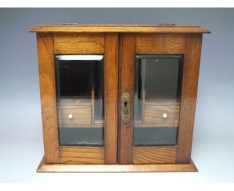 AN OAK SMOKERS CABINET WITH GLAZED DOORS, having fitted interior to include a lidded ceramic jar A/F, H 30 cm, W 34.5 cm, D 1