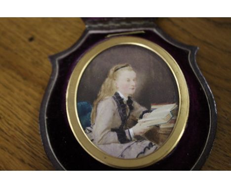 A LATE 19TH / EARLY 20TH CENTURY OVAL PORTRAIT MINIATURE ON IVORY, study of a seated young girl reading a book, set in a shap