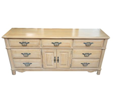 LIGHT ASH SIDE CABINET
with a moulded edge above seven drawers and a pair of central cupboard doors, standing on shaped suppo