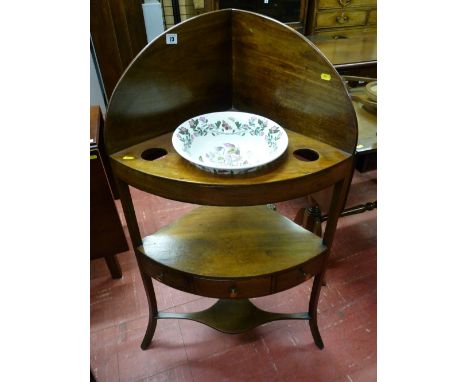 A Sheraton style mahogany corner washstand with top shelf having china recesses and the base shelf with centre opening drawer