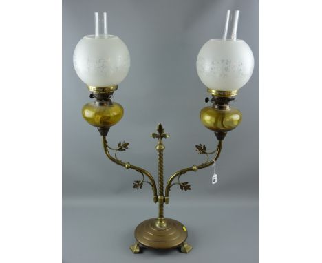 A twin branch brass oil lamp, twist central column on a circular three footed base, leaf adorned arms supporting amber glass 