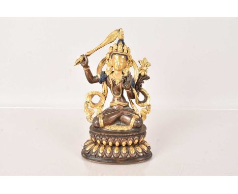 A Tibetan Bronze Buddha figure, in the seated position, the bronze figure heightened in gilt, with blue and red paint decorat