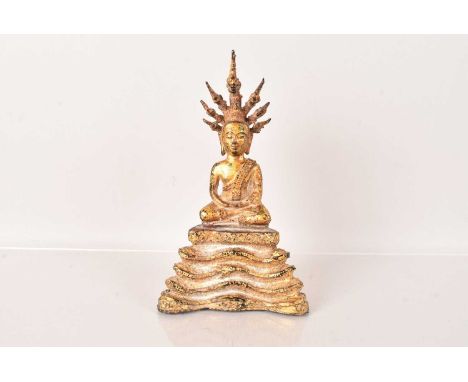 A Bronze figure of a Thai Buddha, seated on a seven headed coiled Naga, known as Mucalinda, the bronze figure covered in gilt