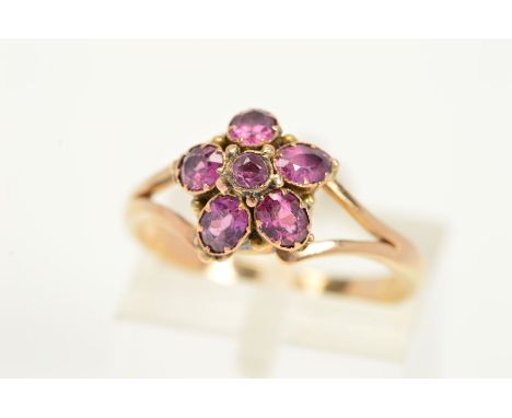 A GARNET CLUSTER RING, designed as a central circular garnet within an oval garnet surround to the bifurcated shoulders, ring