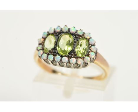 A PERIDOT AND OPAL RING, designed as a line of three graduated oval peridots within a circular opal cabochon surround, ring s