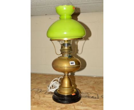 A BRASS OIL LAMP, converted to electricity, standing on a black ceramic base, having lime green glass shade, measuring approx