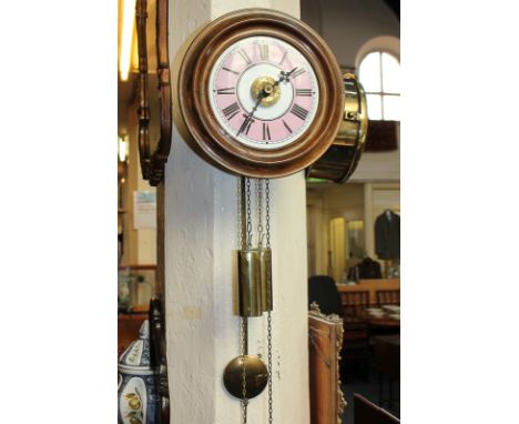A circular wall clock with 7 inch dial, pink coloured chapter ring and Roman numerals, two cylindrical brass weights and pend