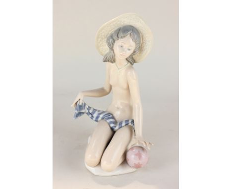 A Lladro porcelain figure of a nude wearing a sun hat, with towel, kneeling beside a beach ball, 23cm