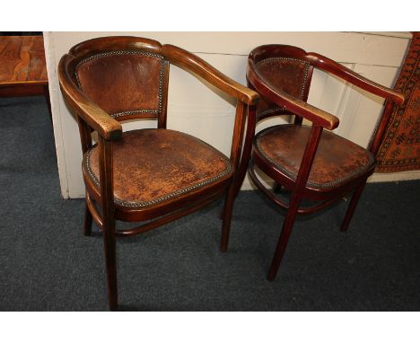 A pair of early 20th century desk chairs with leather panel backs and seats with brass nails, open bow shaped arms