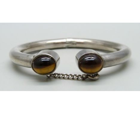 A white metal torque bangle set with two cabochon tigers eye stones, made by a silversmith in Derby in the 1970s, with safety