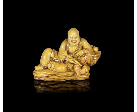 A gilt-decorated soapstone carving of the Laughing Lion Luohan20th centuryThe figure of Xiaoshi Luohan modelled seated at eas