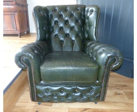 Dark green leather club chair of Chesterfield style, button back with brass stud trim.