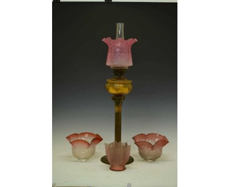 Gilt metal column oil lamp with tinted cranberry glass shade , and three similar shades, 79cm high overall and smaller.