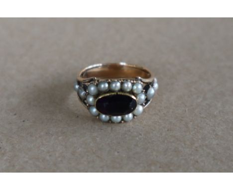 A late George III mourning ring set with a central oval faceted amethyst surrounded by half section pearls, to a yellow metal