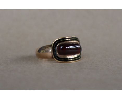 A late George III Mourning ring, with a central cabochon rectangular garnet with black enamel border, to a yellow metal mount