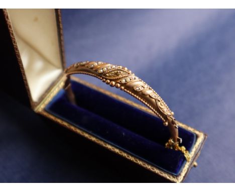 A 9ct gold hinged bangle set with rows of seed pearls and beaded decoration, approximately 8 grams, cased