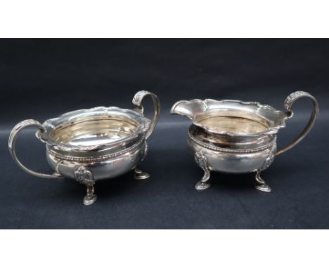 A George V silver cream jug and matching twin handled sugar basin, with a shaped leaf cast edge, beaded body and four pointed