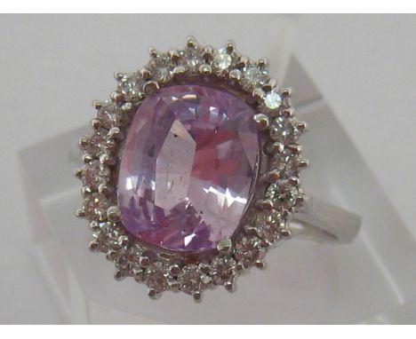 An 18 carat white gold, pink sapphire and diamond cluster ring, the central oval cut stone 10 x 8.2 x 5.1mm (deep), in a surr