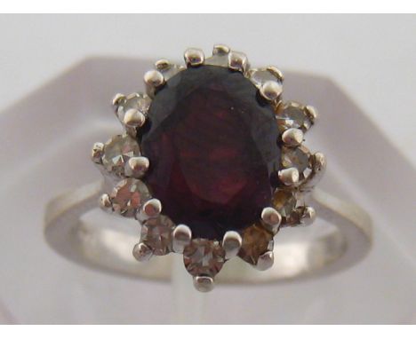 A garnet and diamond cluster ring, the central oval stone 8.2 x 6.7mm, in a surround of brilliants, the white gold mount stam