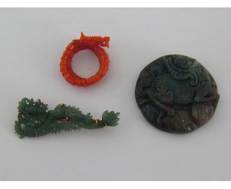 A finely carved red coral ring, modelled as a coiled dragon, finger size K, together with a jade brooch mounted in yellow gol