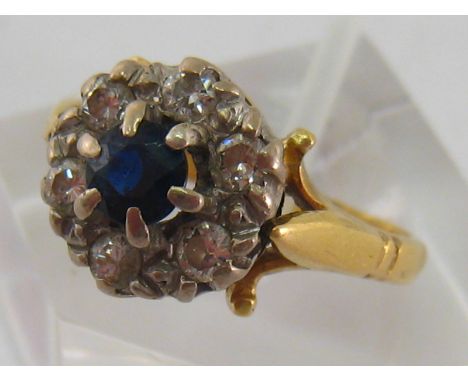An 18 carat gold, diamond and sapphire cluster ring, the dark central round cut sapphire 4.5mm diameter, in a surround of bri