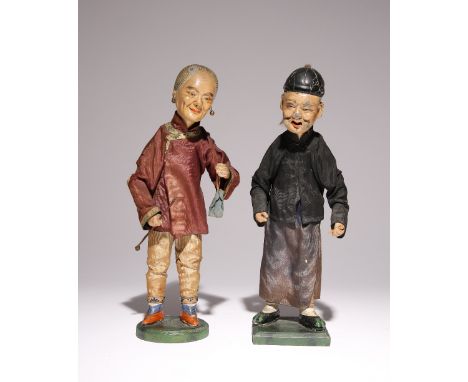 A PAIR OF CHINESE DOLLS 19TH CENTURY Standing on wooden bases, clothed in Chinese garments, the woman holding a purse and a c
