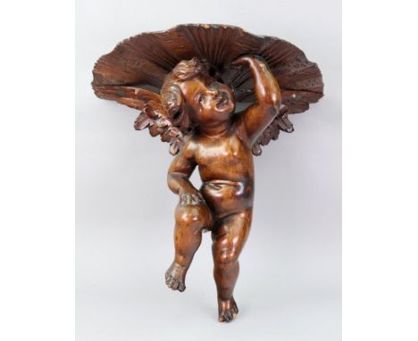 An Italian stained pine wall bracket, second half 19th century, carved in the form of a cherub holding a carved demi lune she
