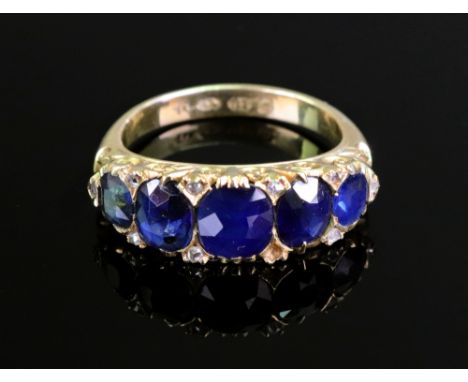 A late Victorian gold and sapphire five stone carved half-hoop ring with rose diamond points, the graduated cushion-shaped st