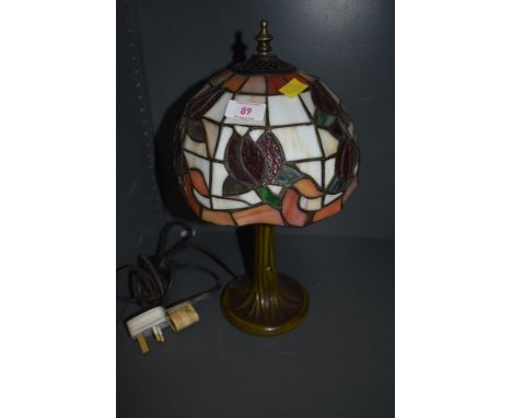 A stained glass table lamp having Tiffany style shade and metal base styled as a tree trunk.