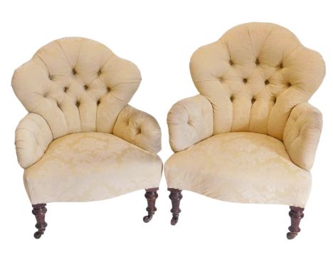 A pair of Victorian low seated button back upholstered arm chairs, in gold damask silk, on turned mahogany legs, and with pot