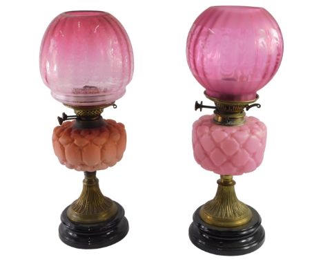 A pair of late Victorian brass oil lamps, with coloured satin glass button cushion effect reservoirs, one in pink and one in 